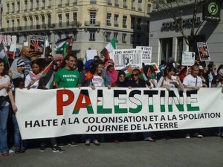 Photo de manifestants portant banderolle protestant contre occupation et spoliation de la terre en Palestine.