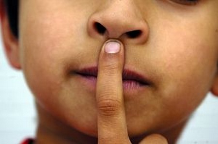 Photo du bas de visage d'un enfant indiquant du doigt sur bouche le silence.