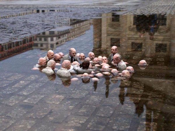 Photo symbolique de bustes humains au milieu de flaque eau avec reflets de bâtiments.
