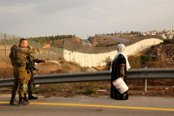 Photo de femme palestinienne avec seau devant soldats israliens.