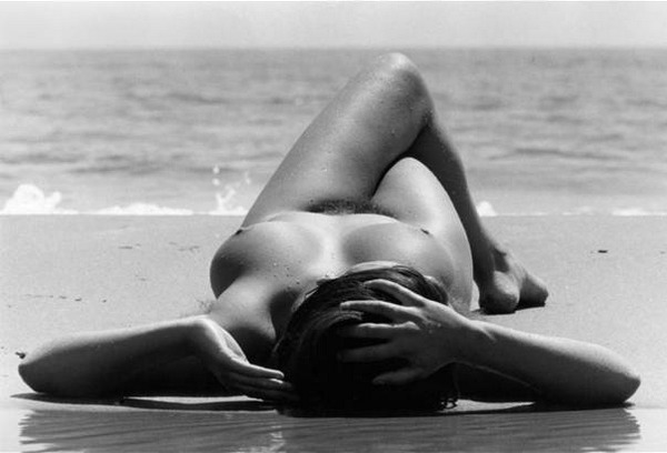 Photo de corps féminin anonyme, allongé, nu, sur une plage, face à la Mer.