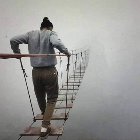 Photo d'homme marchant sur un pont de corde en plein brouillard.
