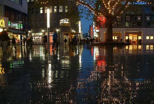 place citadine, éclairée par commerces, vue de nuit avec reflets sur pluie